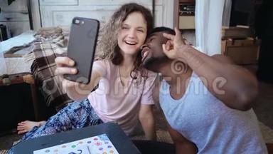 快乐的多民族夫妇在智能手机上自拍照片。 穿睡衣的女人和男人做滑稽的表情，玩得开心。